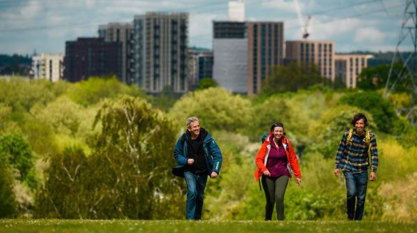 Three walks on an uphill ascent on Hampstead Heath with city buildings in the background.